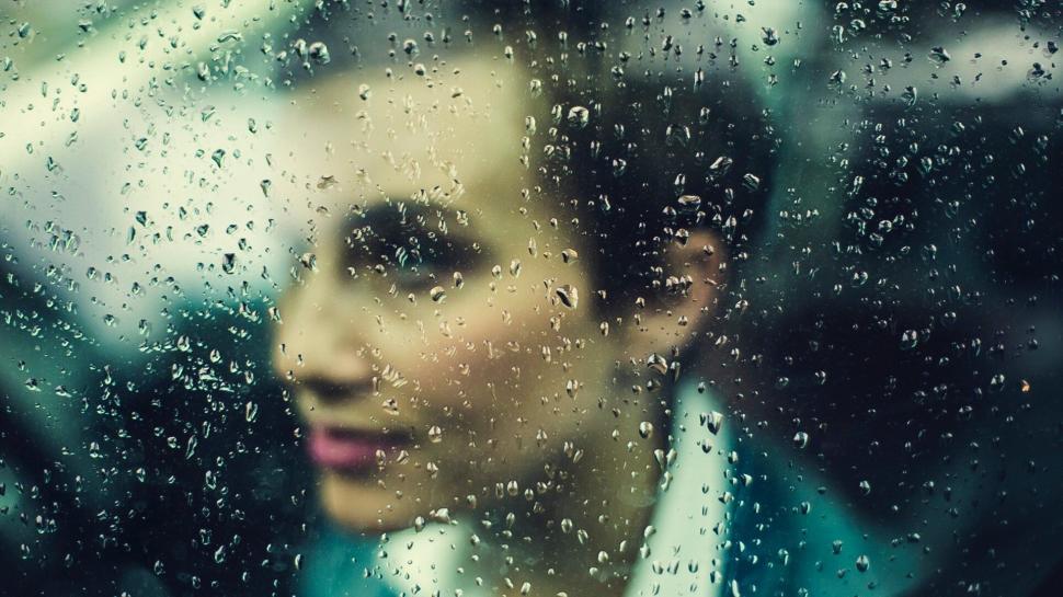 Free Image of Raindrops on window with blurred face behind 