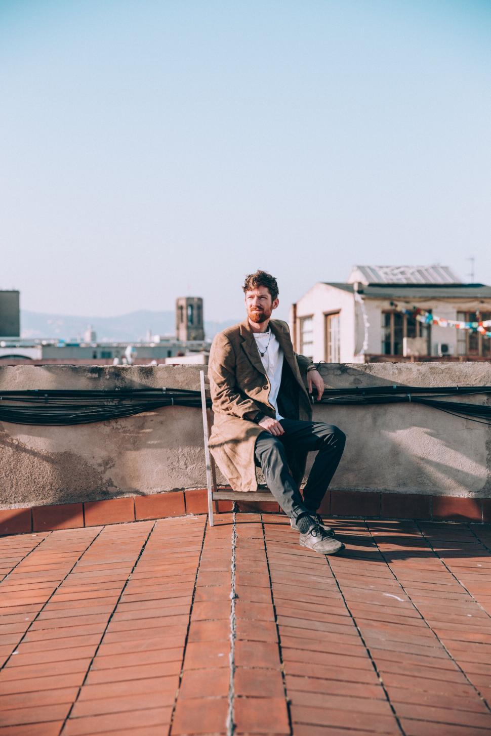 Free Image of Man sitting on rooftop against city 
