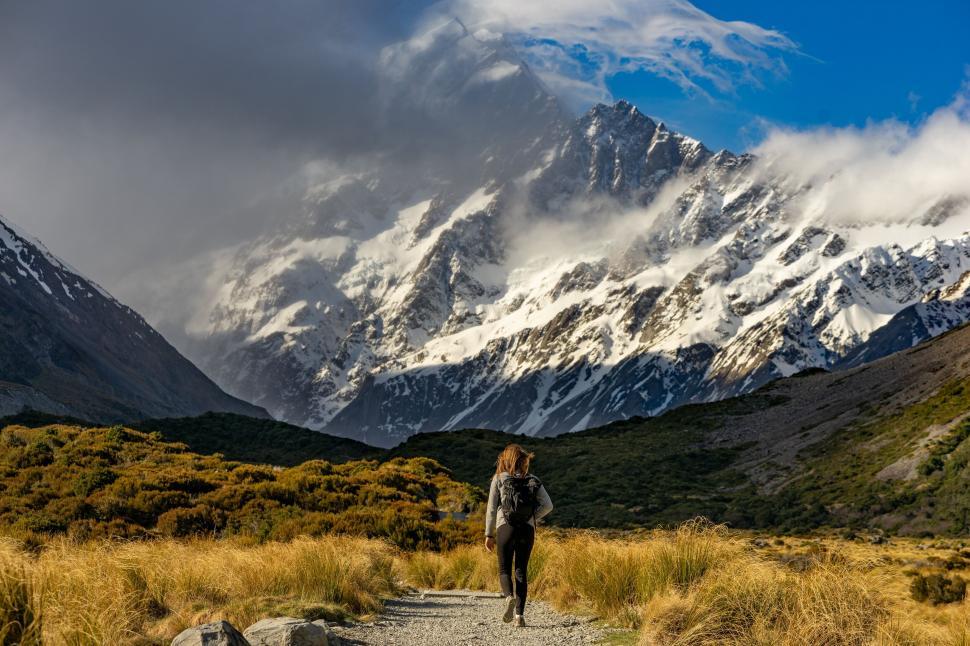 Free Image of Woman hiking towards mountain under cloudy sky 