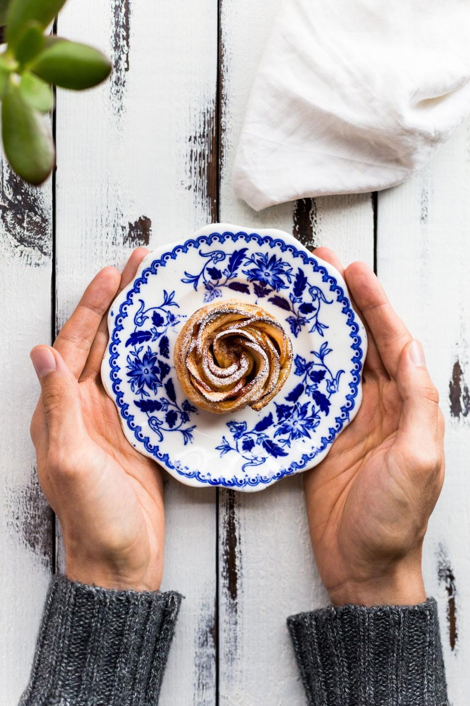 Free Image of Hand holding cinnamon roll on decorative plate 