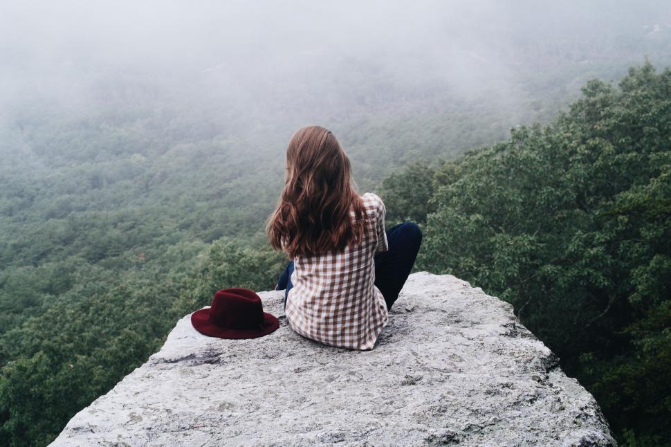 Free Image of Woman sitting on edge overlooking foggy forest 