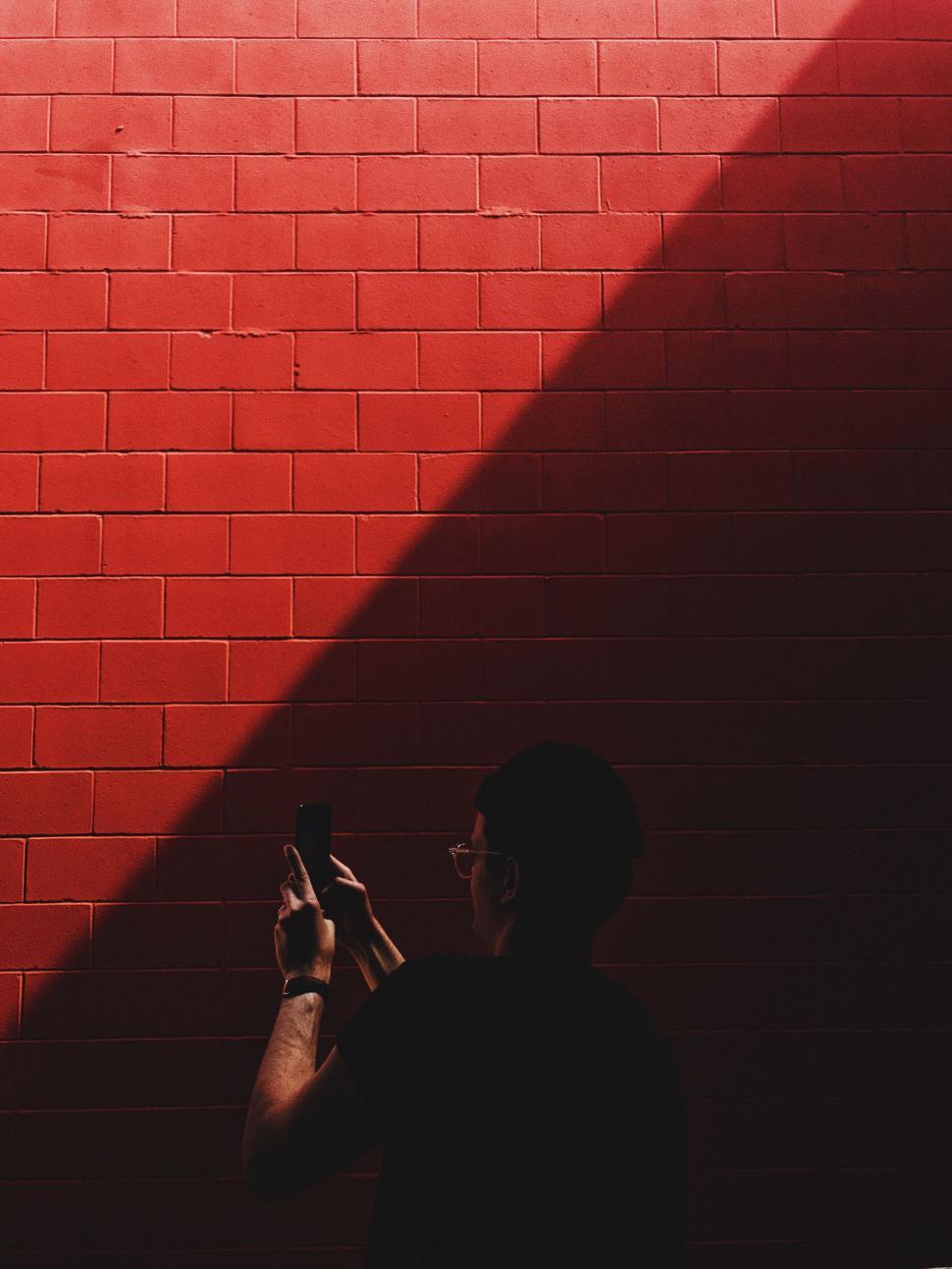 Free Image of Man photographing shadow on vivid red wall 
