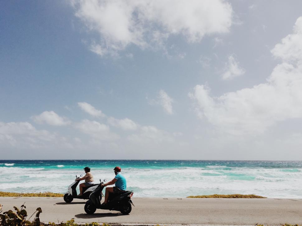 Free Image of Scooter riders enjoying a beachside road 