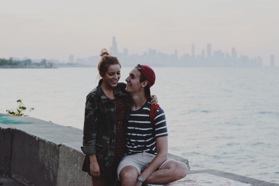 Free Image of Couple kissing on lakefront with cityscape 