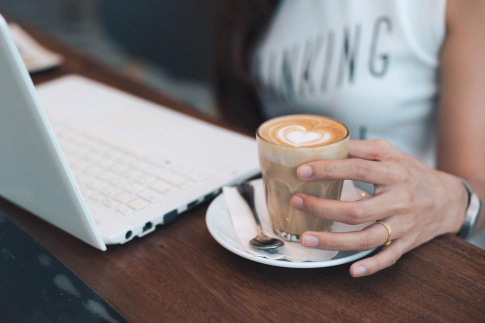 Free Image of Woman holding a cappuccino at a cafe 