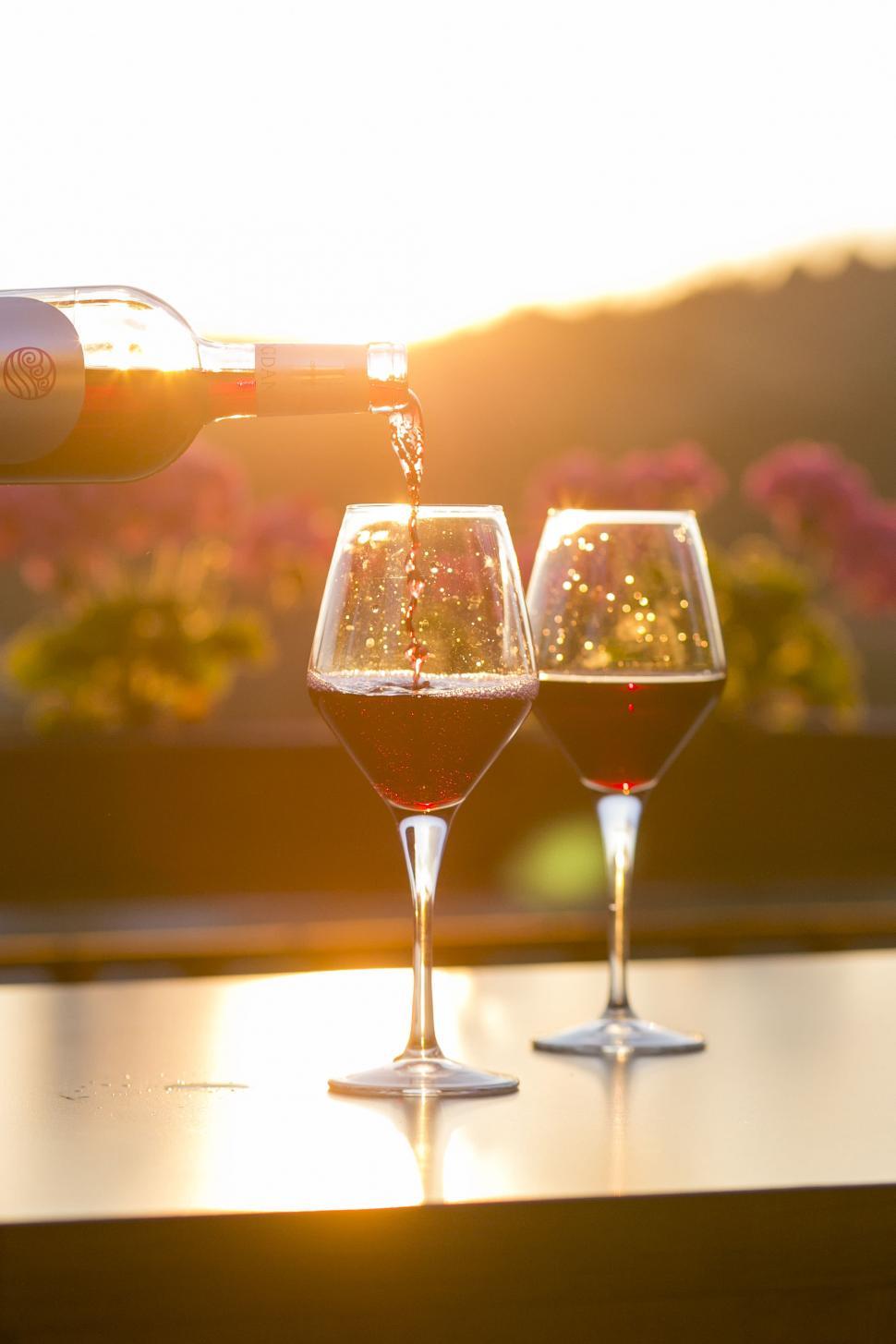 Free Image of Red wine pouring into glasses at sunset 