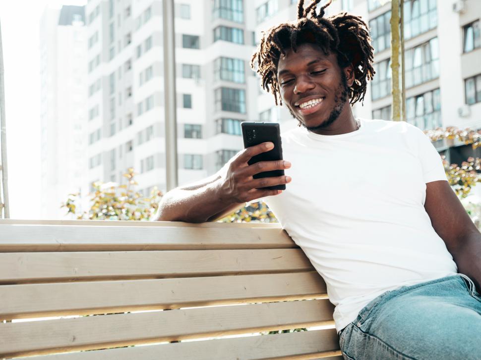 Free Image of A man sitting on a bench looking at a phone 