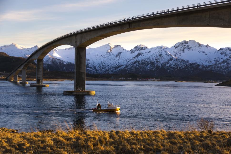 Free Image of A bridge over water with a boat and mountains in the background 