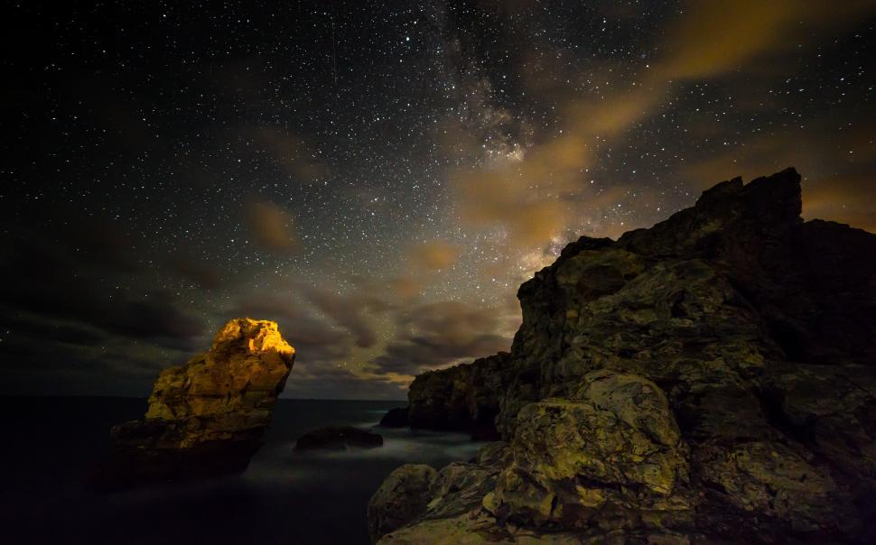 Free Image of A rocky shore with a bright light at night 