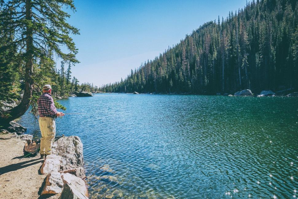Free Image of Fisherman by the lake in a serene mountain setting 
