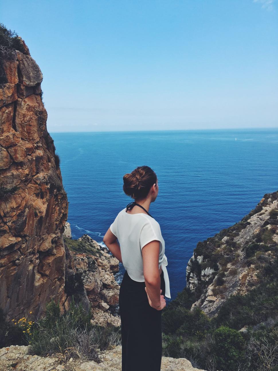 Free Image of Woman standing on cliff overlooking the sea 