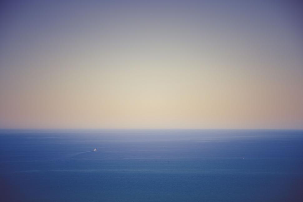 Free Image of Sunset over calm ocean with small boat visible 