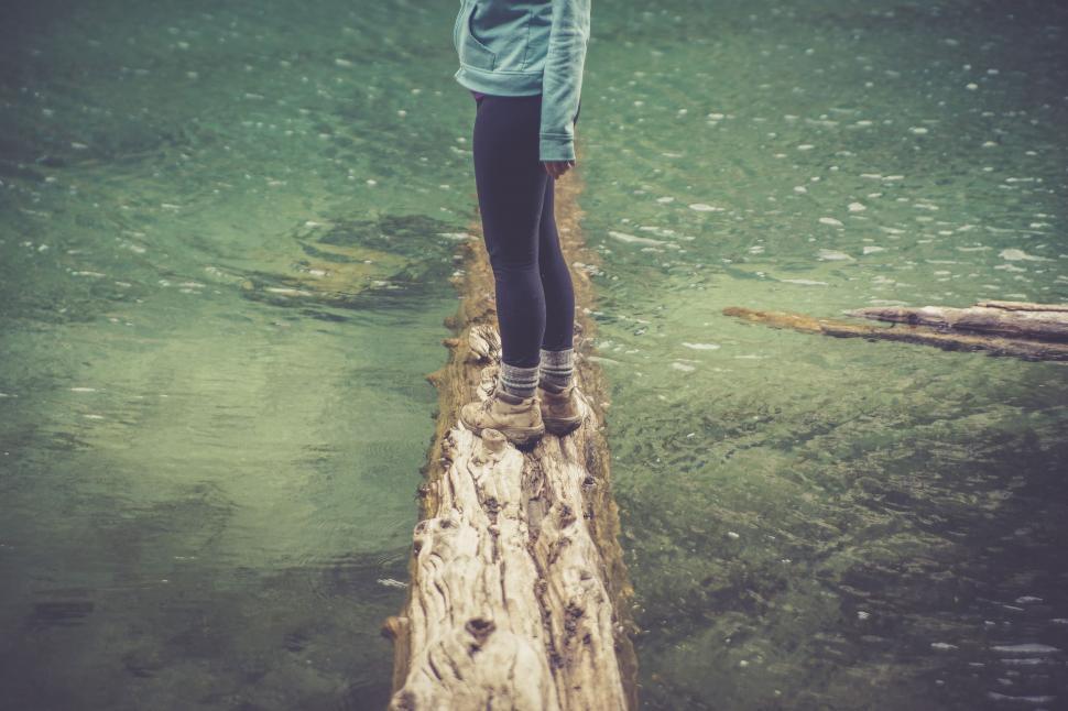 Free Image of Trekker balancing on a log over a turquoise river 