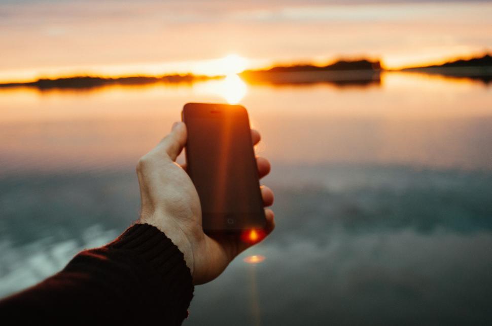 Free Image of Hand holding smartphone capturing sunset 