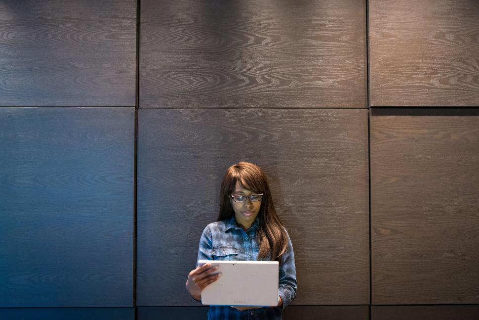 Free Image of Woman reading tablet in front of wooden wall 