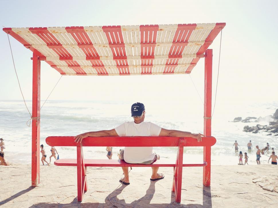 Free Image of Man sitting under beach hut on sunny day 