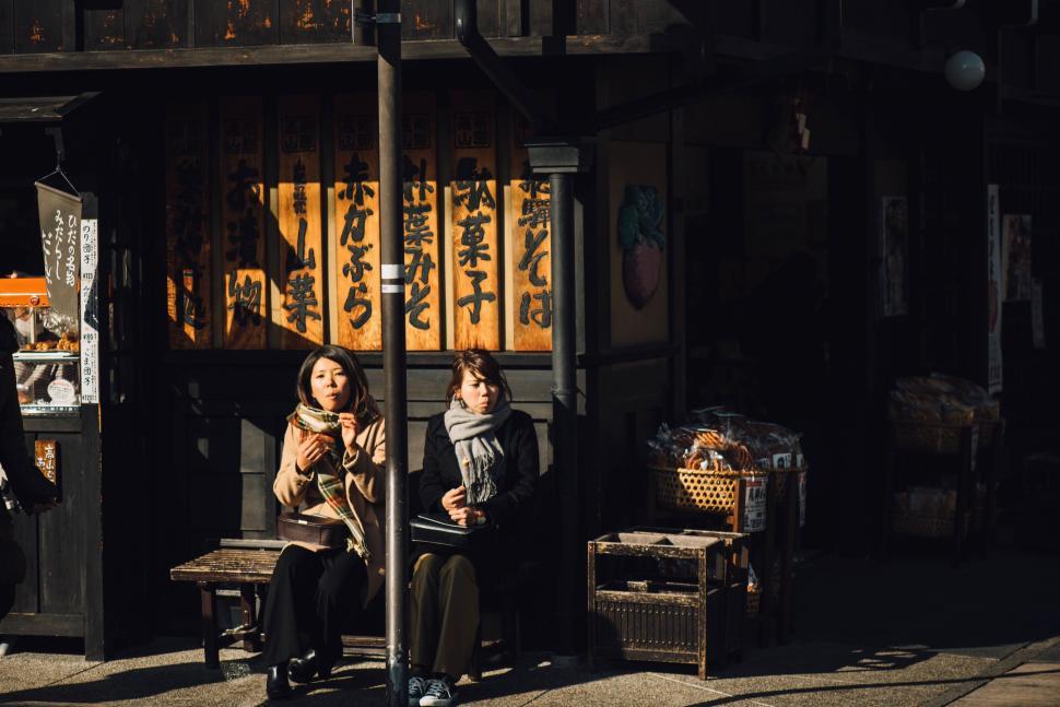 Free Image of Two women sitting by a traditional shop 