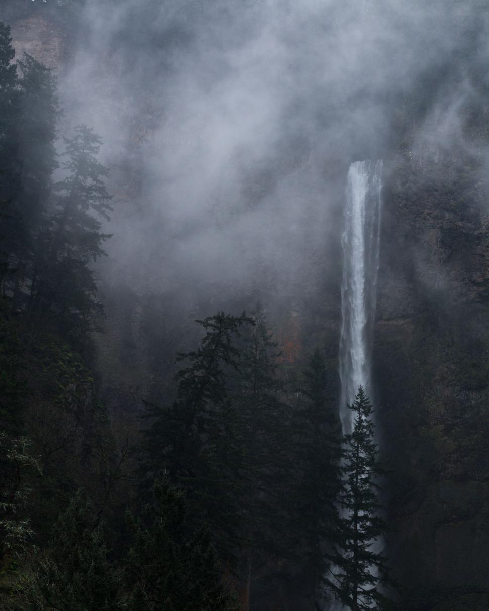 Free Image of Majestic waterfall amidst misty forested mountains 