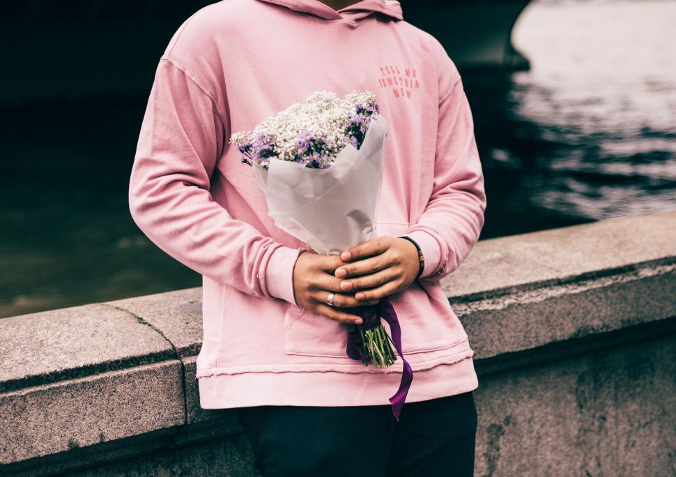 Free Image of Person holding flowers in a pink hoodie at a bridge 