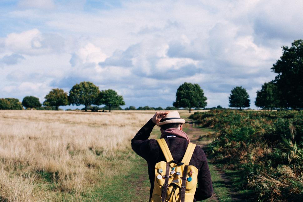 Free Image of Man with backpack and hat walking in an open field 