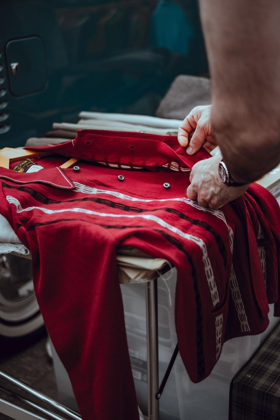 Free Image of Man folding red vintage jacket on suitcase 