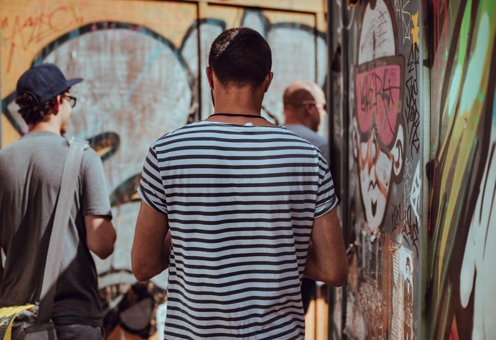 Free Image of Man in striped shirt looking at graffiti wall 