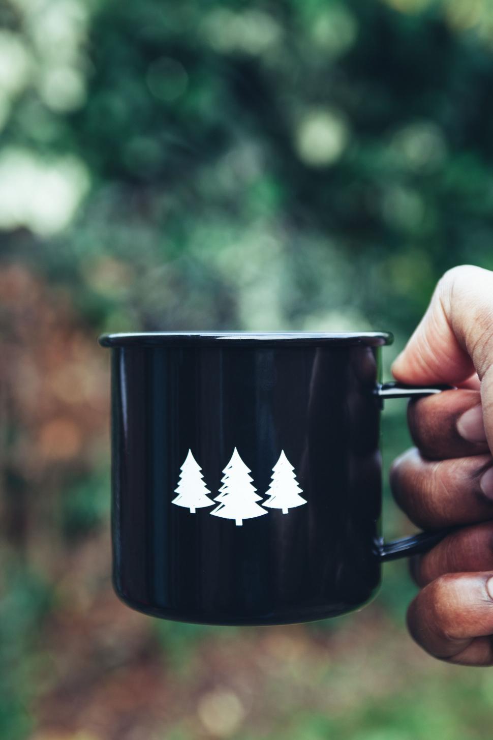 Free Image of Hand holding a black camping mug with tree logo 