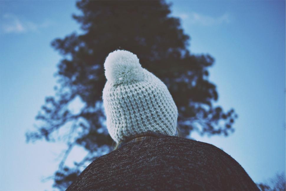 Free Image of Person in white beanie gazing up at tree 