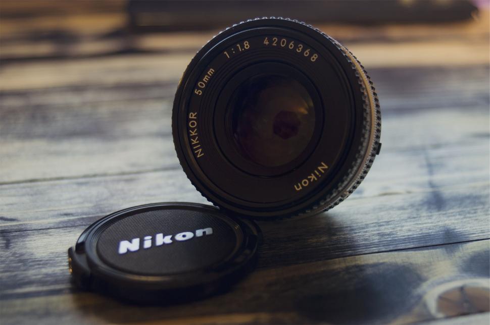 Free Image of Close-up of Nikon lens and cap on wooden table 