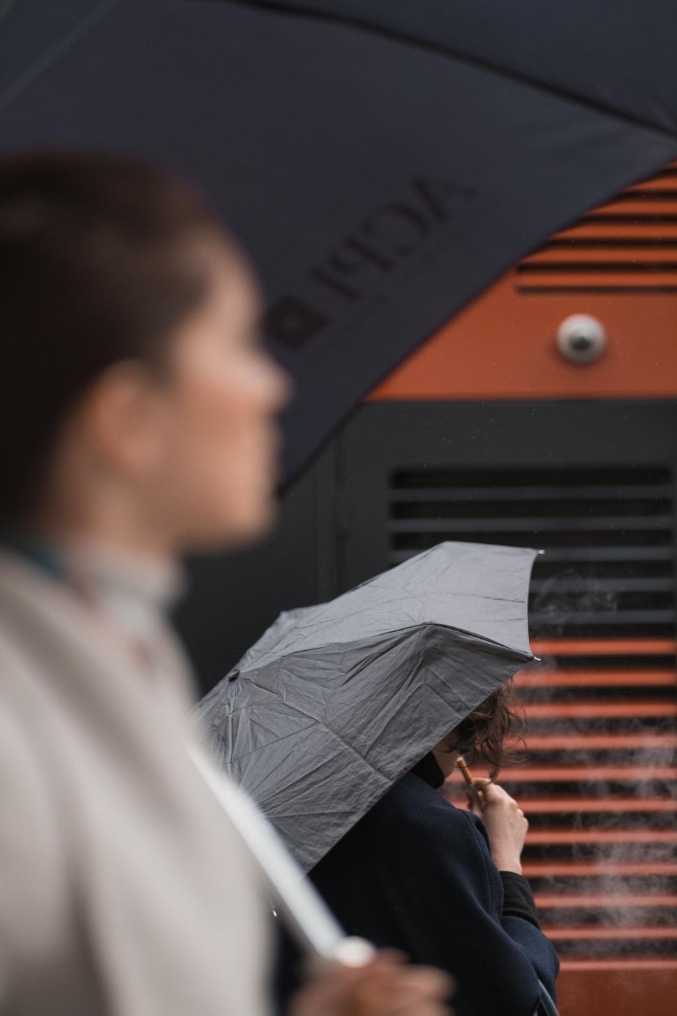 Free Image of Woman under umbrella by orange building 