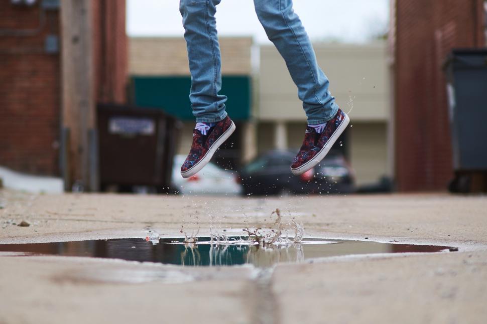 Free Image of Person jumping over a puddle on the street 