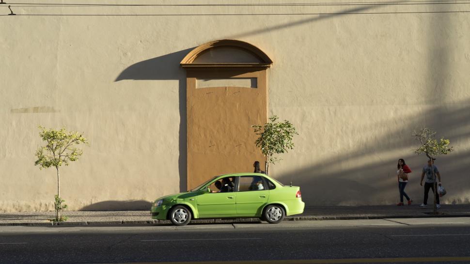 Free Image of Green car parked by a yellow wall in sunlight 