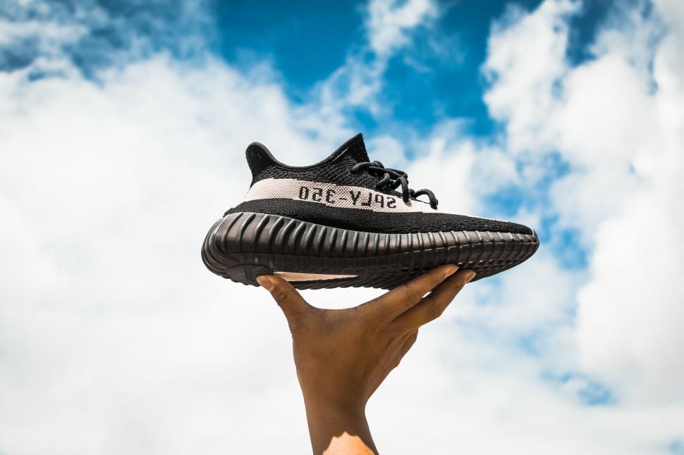 Free Image of Hand holding sneaker against cloudy sky 