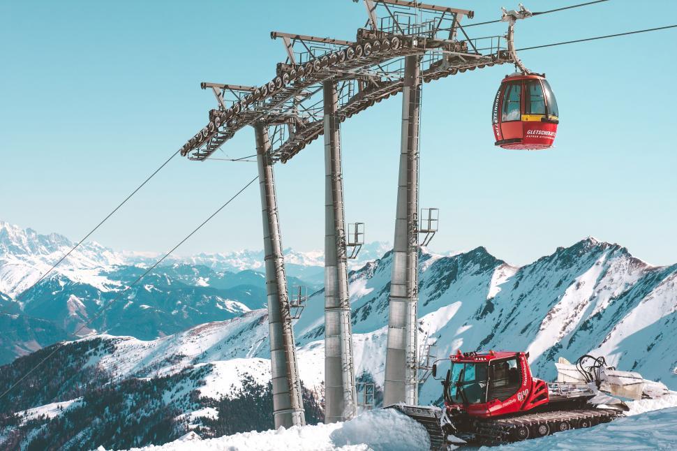 Free Image of Snowy mountain ski lift with red gondola and piste machine 
