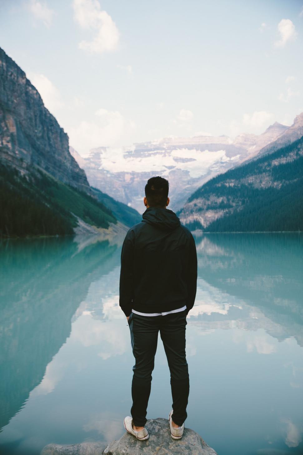 Free Image of Man gazing at mountain lake from rock 