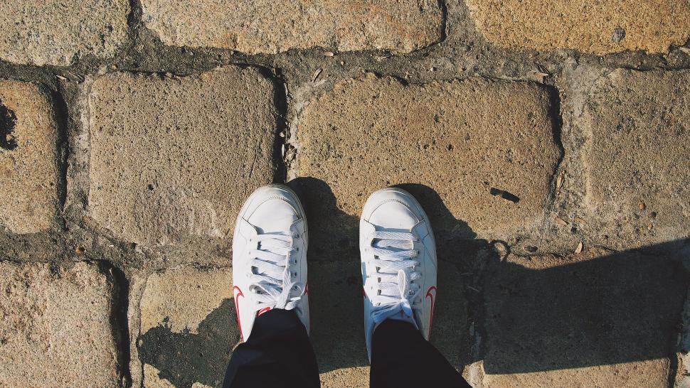 Free Image of White sneakers on classic cobblestone pavement 