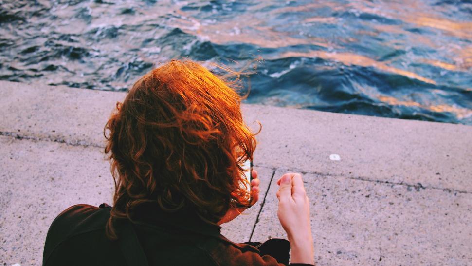 Free Image of Redhead woman sitting by the sea at sunset 