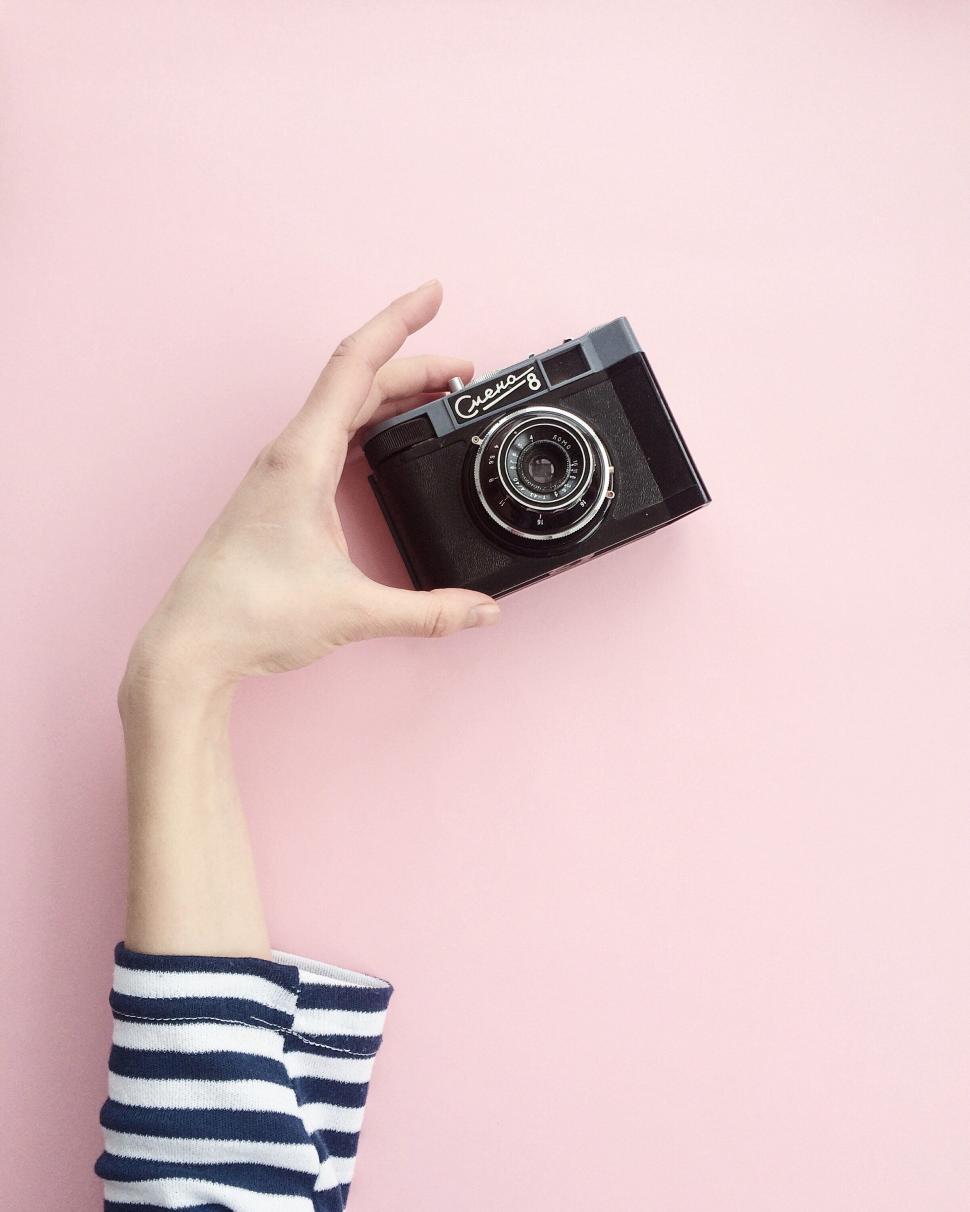 Free Image of Hand holding a classic camera against a pink backdrop 