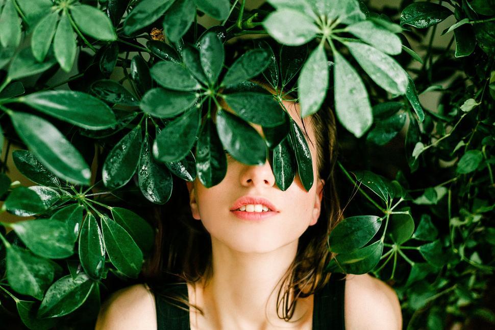 Free Image of Enigmatic woman peeking through lush greenery 