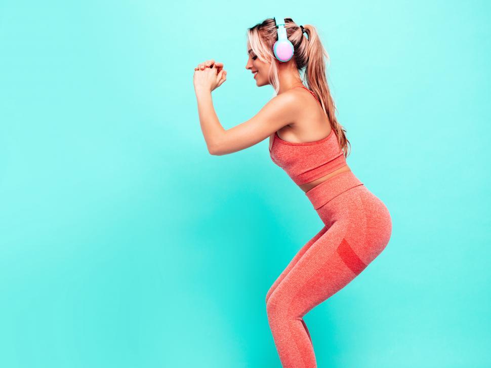 Free Image of A woman wearing headphones and squatting 