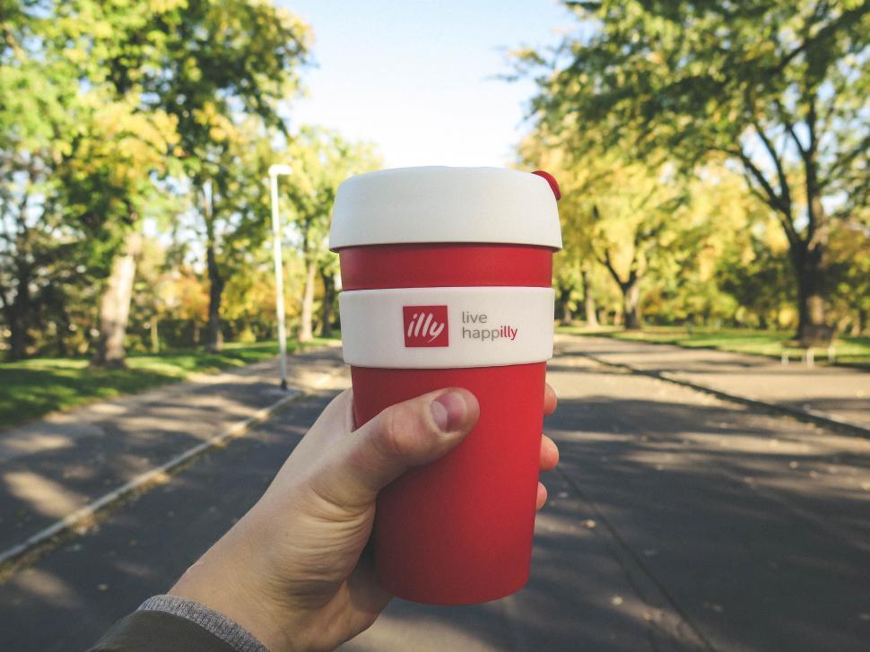 Free Image of Hand holding a red Illy coffee cup in park 