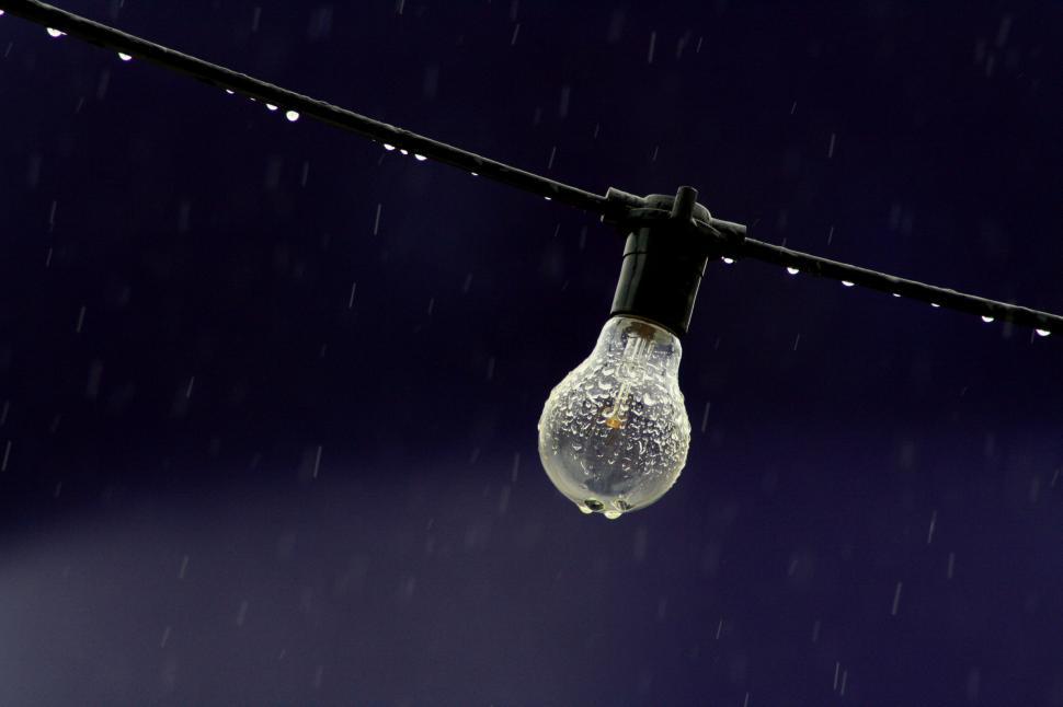 Free Image of Light bulb glistening in the rain on wire 