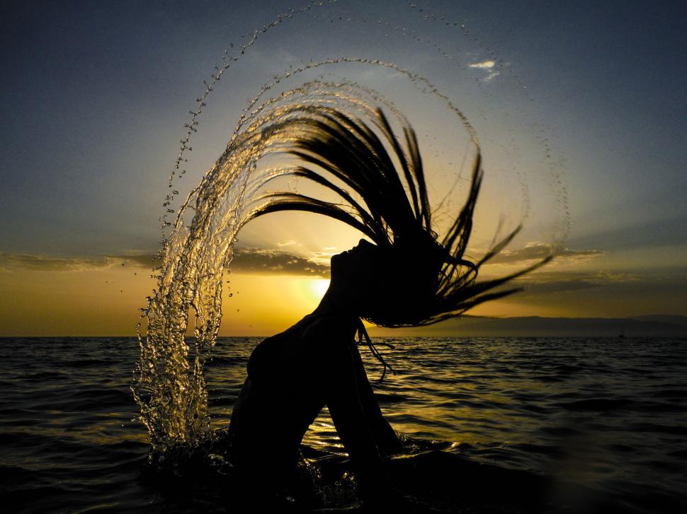 Free Image of Silhouette of a woman flipping wet hair in sunset 