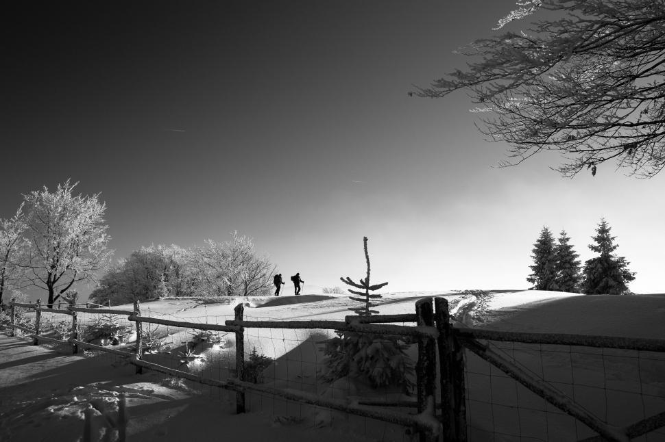 Free Image of Snowy landscape with a couple walking alongside a fence 