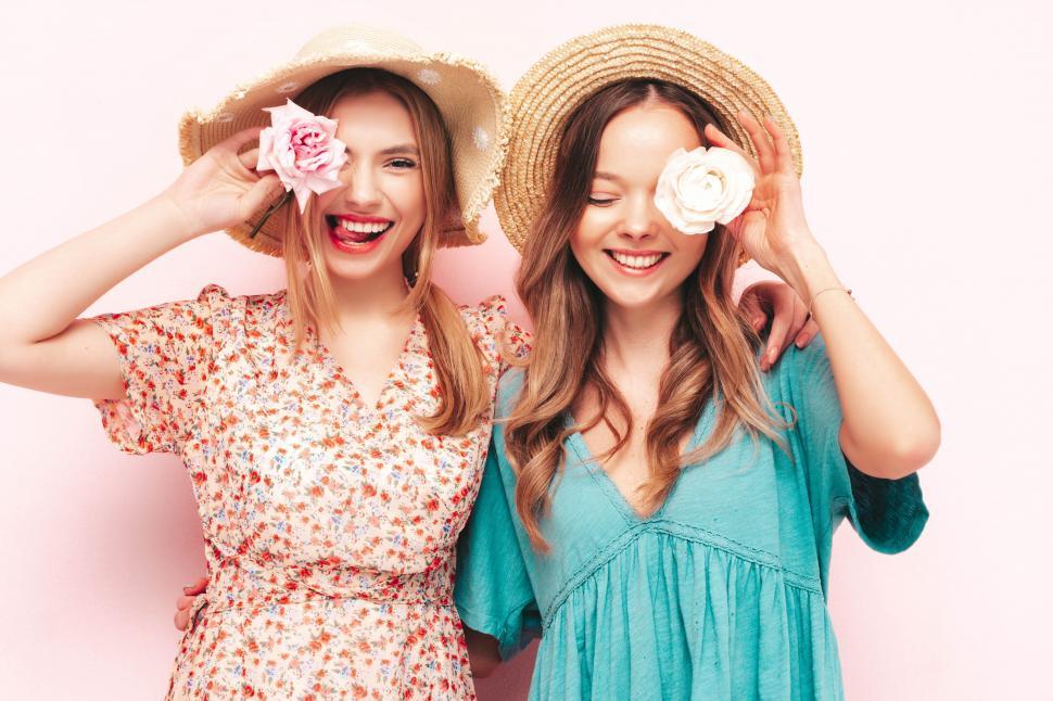 Free Image of Two women wearing hats and holding flowers over their eyes 