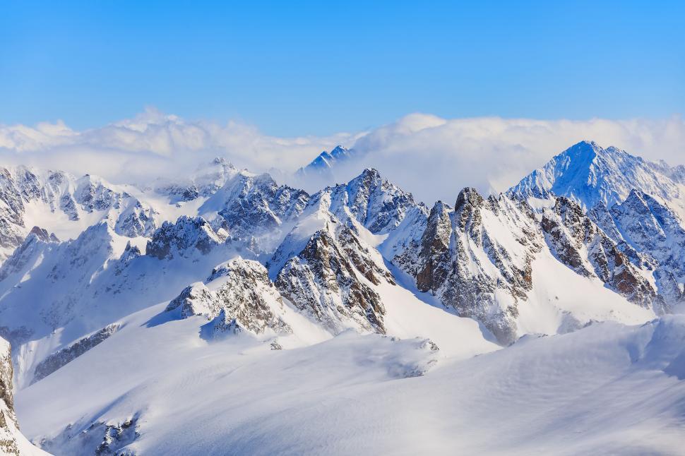 Free Image of Snow-covered jagged mountain range rising above clouds 