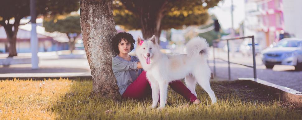 Free Image of Woman with dog leaning on tree in urban park 