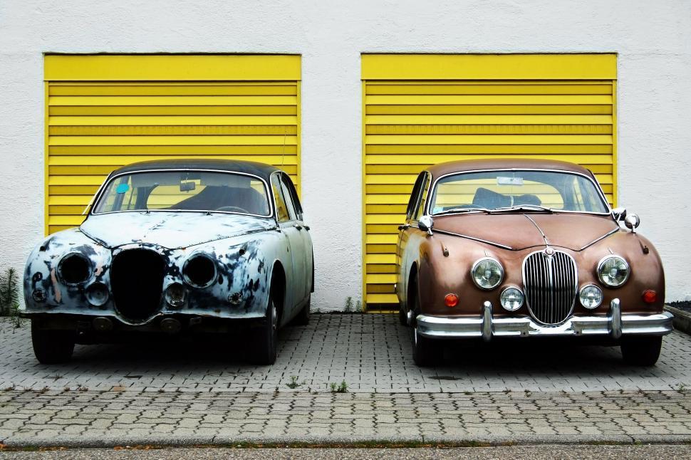 Free Image of Two vintage cars parked by yellow garages 