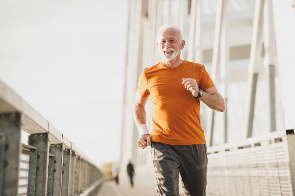 Free Image of Senior man jogging on bridge in orange shirt 
