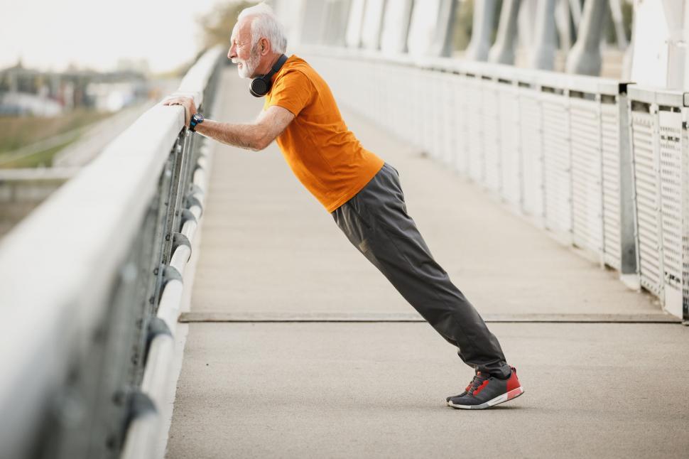 Free Image of Elderly man exercising on a bridge railing 